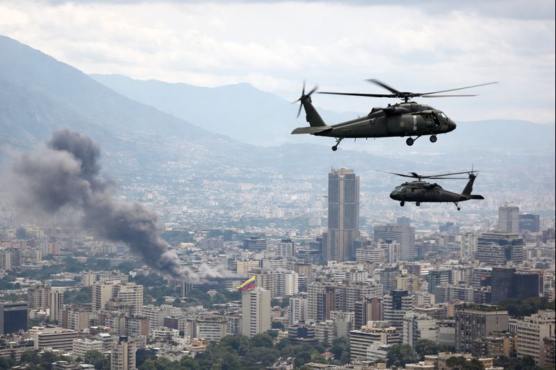 U.S. military helicopters fly over Caracas as smoke rises from the city during reported strikes in Venezuela in January 2026.