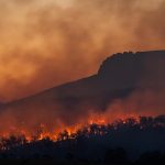 Wildfire burning across a hillside at dusk in southern Europe, with thick smoke rising near Madrid and Bordeaux