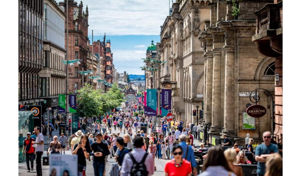 Crowds fill a busy Glasgow city street decorated with Commonwealth Games banners during Glasgow 2026