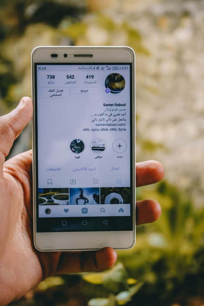 A hand holding a smartphone showing a social media profile screen outdoors