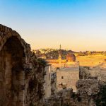 Vivid sunset view of Jerusalem's Old City through an ancient stone arch, evoking the Ark of the Covenant discovery