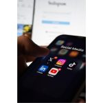 Person holding a smartphone showing TikTok, Instagram, X, LinkedIn and YouTube app icons under a folder labeled Social Media